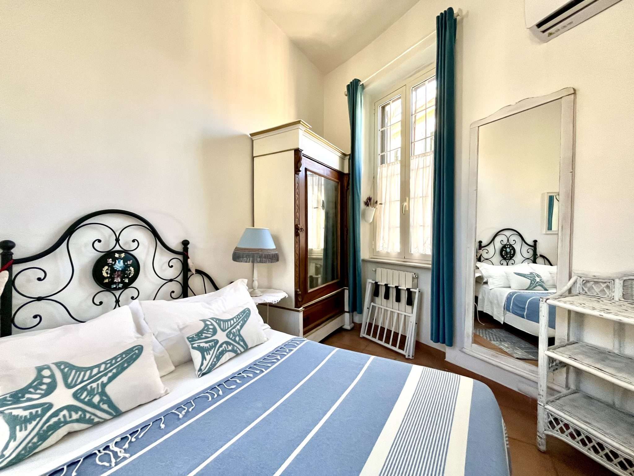 Interno di una camera a Ostia a tema marino con letto in ferro battuto e cuscini con stelle marine Titolo immagine: interni-camera-